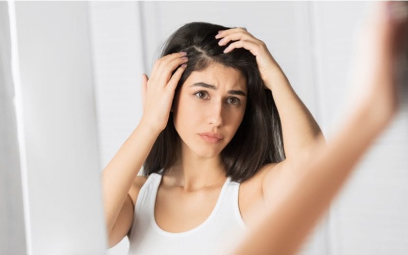 Image of a dark haired woman standing spreading her hair roots looking for dandruff before using an apple cider vinegar hair rinse