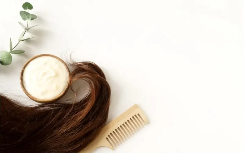 To help answer "how often should you do a hair mask" sits a product next to a plant with a wooden comb in a lay flat image