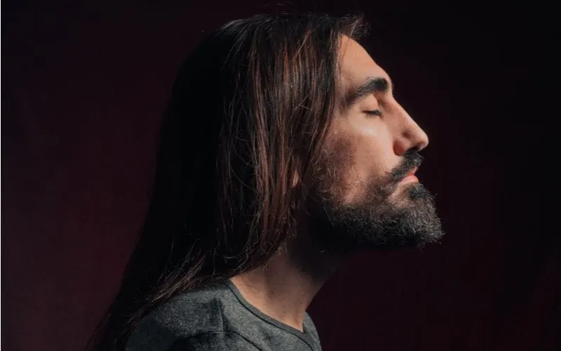 Man rocking a long hairstyle for men looks ahead and closes his eyes in a side profile