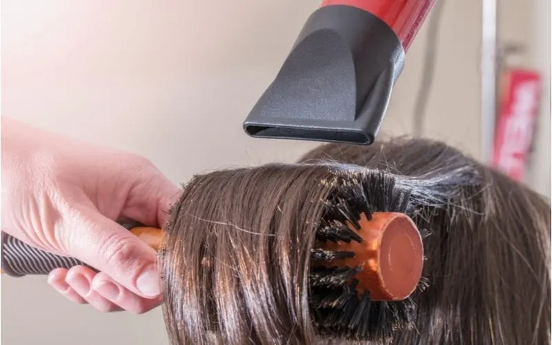Woman getting a blowout with someone using a boar bristle brush along with a hair diffuser