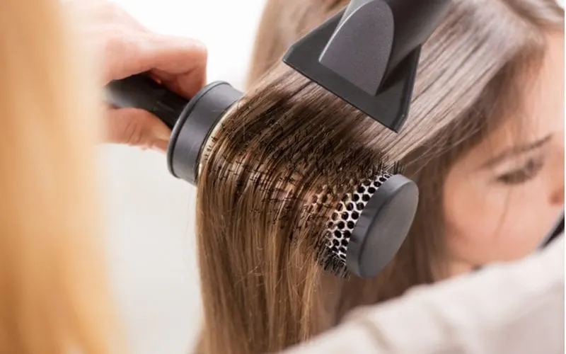 For a piece on what is a hair blowout, a woman getting one in a salon using a round brush and a hair smoother