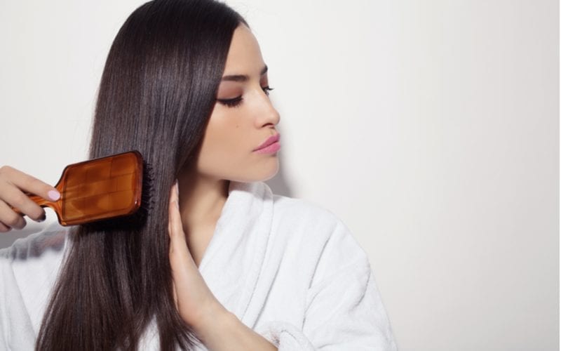 Woman brushing her hair with a wooden brush in a white robe for a piece on what is a hair mask