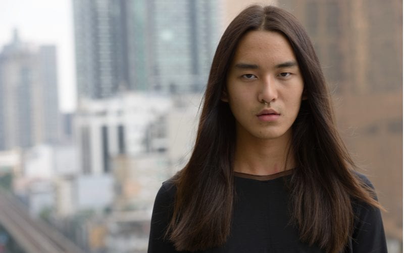 Long-haired asian man stands on a balcony with the skyline in the background