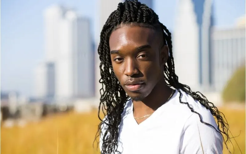 African-American man stands in front of a skyline wearing a long hairstyle for men and a white vneck