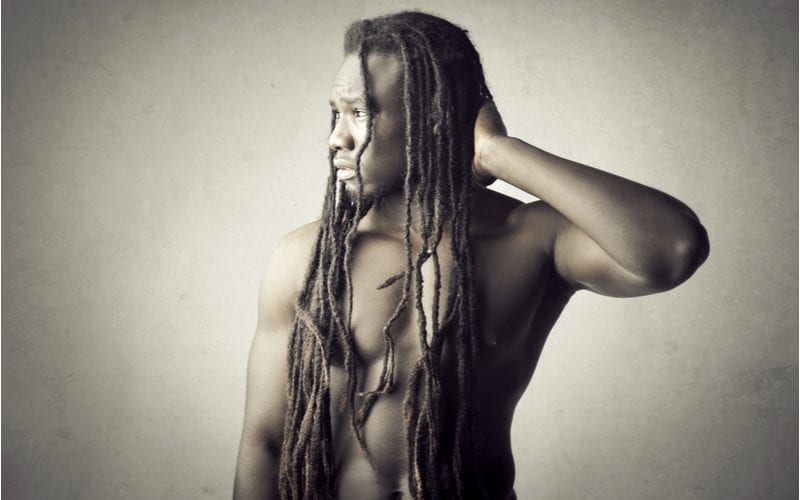 African American man with locs stands shirtless and holds the back of his head