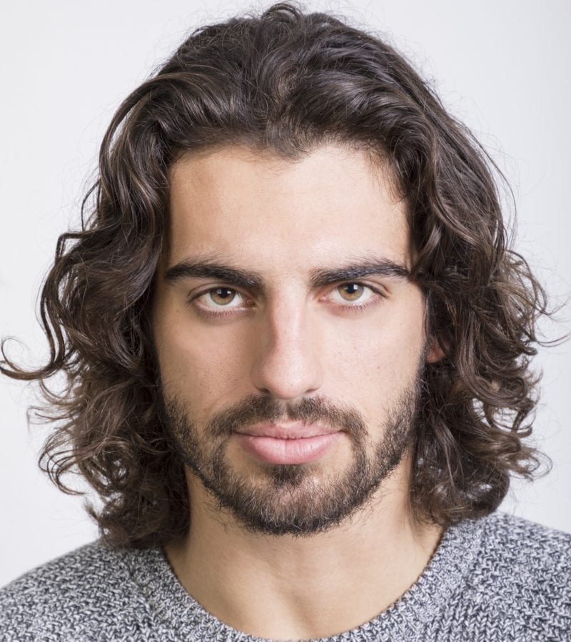 Arabian looking man with long hair looks directly at the reader while wearing a long haircut for men