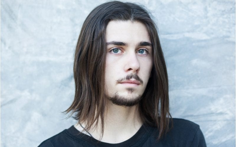 Man with whispy ends and long hair with a gross goatee and mustache looks at the camera without smiling