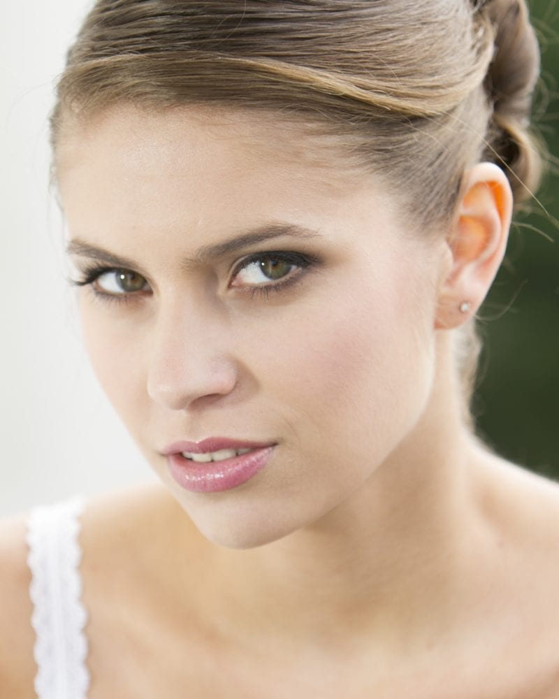 Woman with a pulled-back hairstyle in a white lace camisole looks at the camera from the corner of her eye