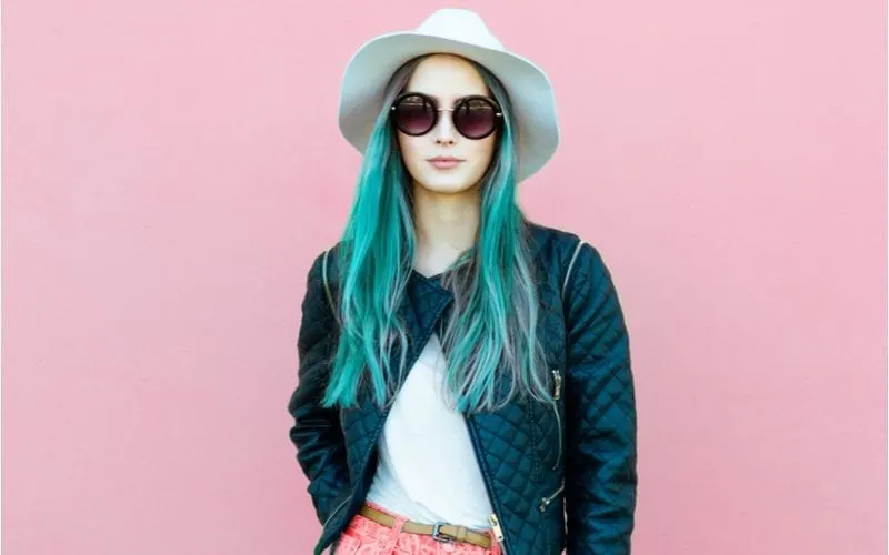Woman with semi-permanent hair color for a piece on what is it stands in sunglasses and a boho hat and a jean jacket