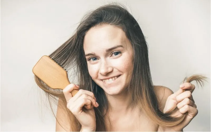Woman with fine hair holding a brush in one hand and the tips of her hair in the other