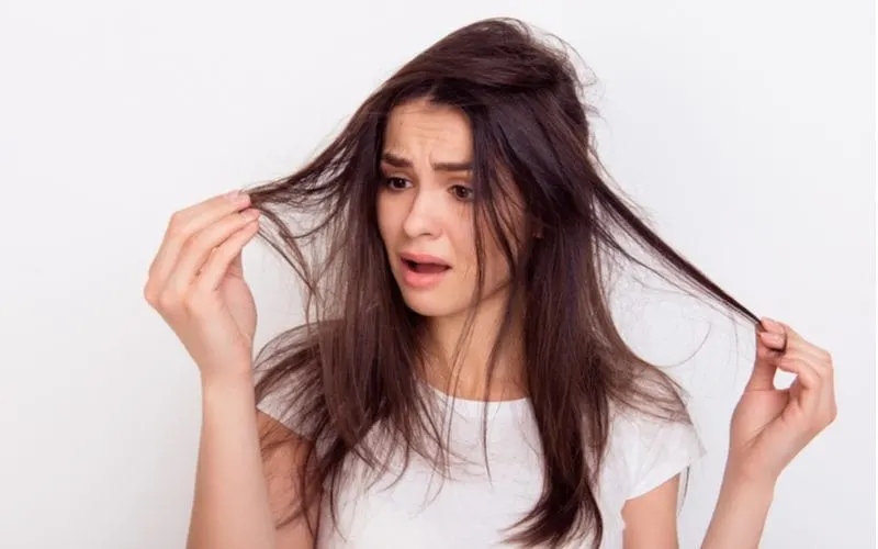 To help answer the question what is hair porosity, a woman standing in a white room holding her damaged hair because she didn't read our guide