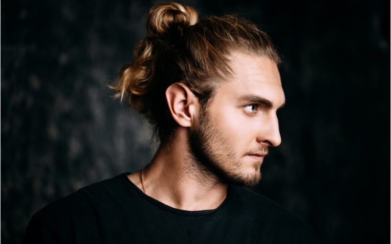 Man with a long man bun put up in his hair seriously looks to his left in a darkened room
