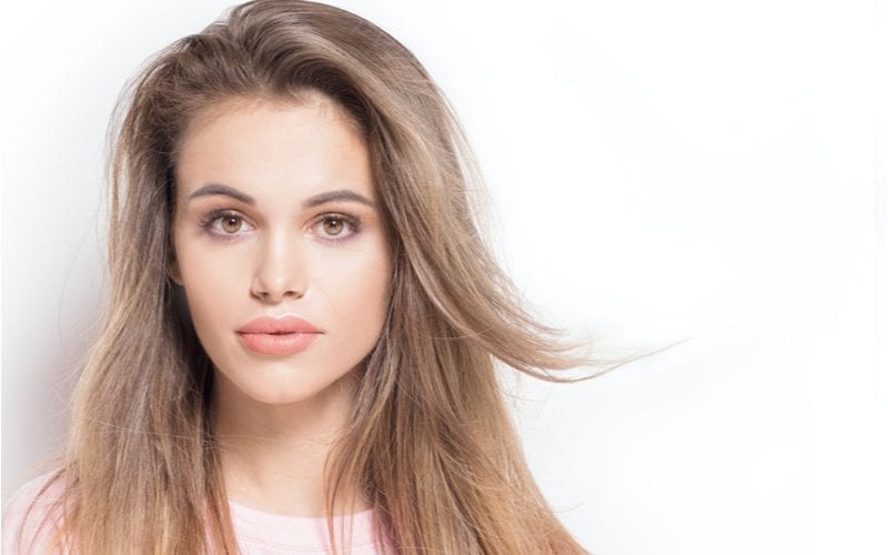 Woman with ash brown hair in a studio lets the locks blow to the left while smirking slightly