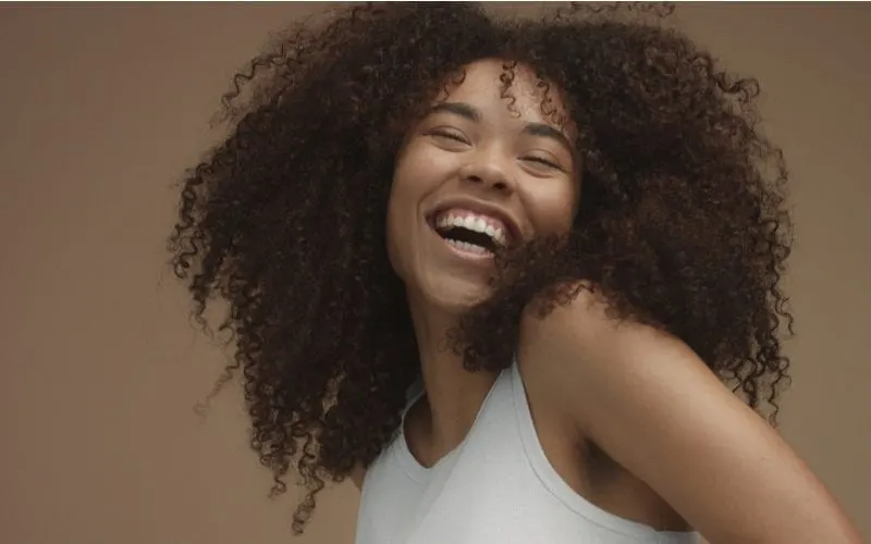 Lady with afro hair lets it all flow while smiling big and wearing a white tank for a post on is coconut oil good for hair