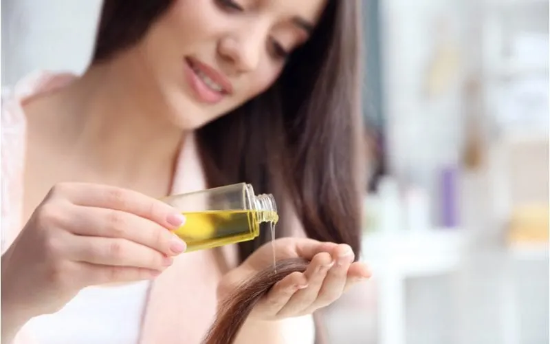 For a piece on what is hair serum, a brunette woman pouring some of the oil into her hand while standing in a white shirt with a blurry background