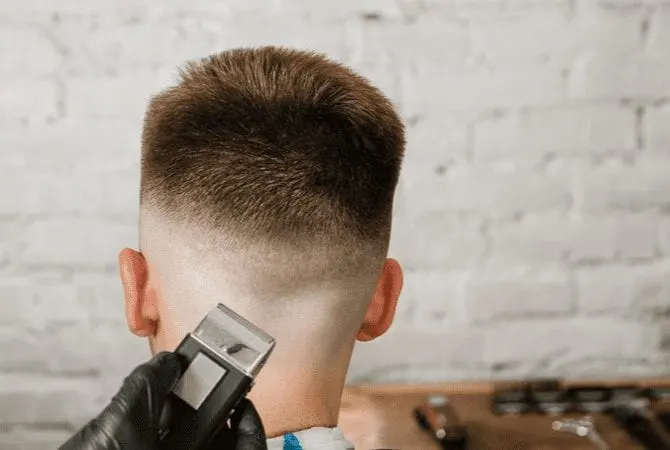 Man in a stylist's chair looks towards a brick wall and gets a medium type of fade haircut from a gloved stylist