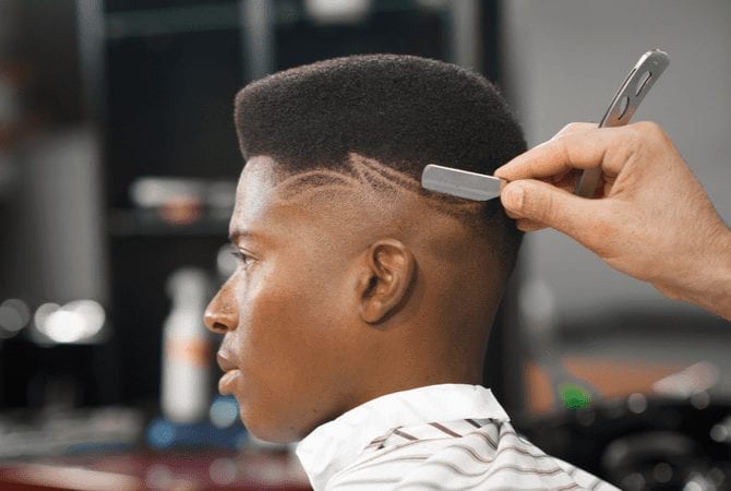 Afro-American man with a high top fade sits in the barber chair and gets a straight razor shave
