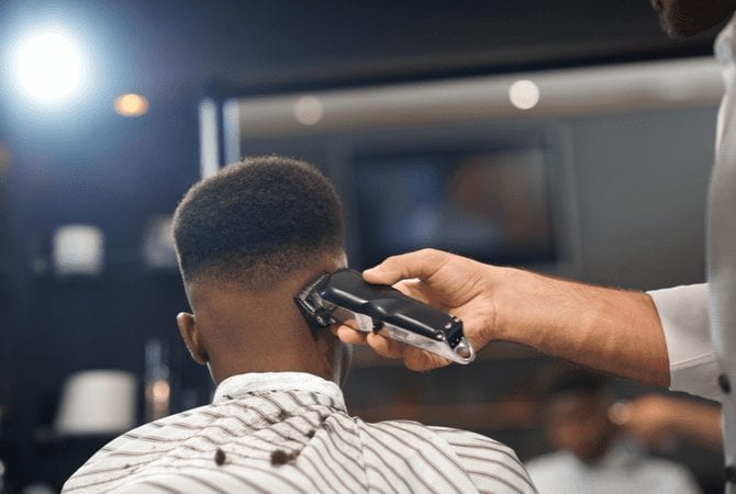 High drop skin fade being put on a black man in a barbershop wearing a striped cape