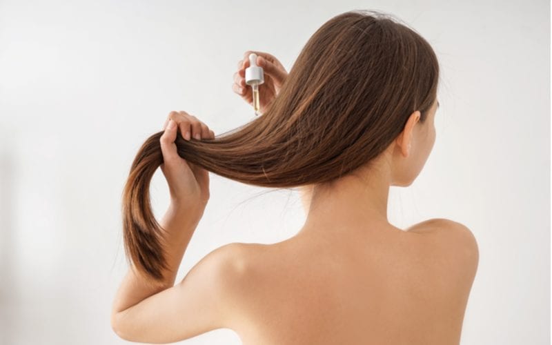 Behind shot of a woman using hair serum while holding her hair in her left hand and looking right