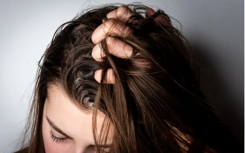 Middle-aged girl holds her hair between fingers that are greasy because she did not read our guide on what is hair serum