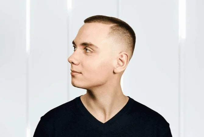 Man in a black shirt with a skin fade that turns into a buzzcut looks up to his right