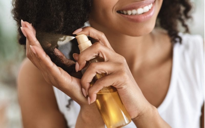 For a piece on what is the best oil for hair, a woman with natural hair spraying a bottle onto the curls