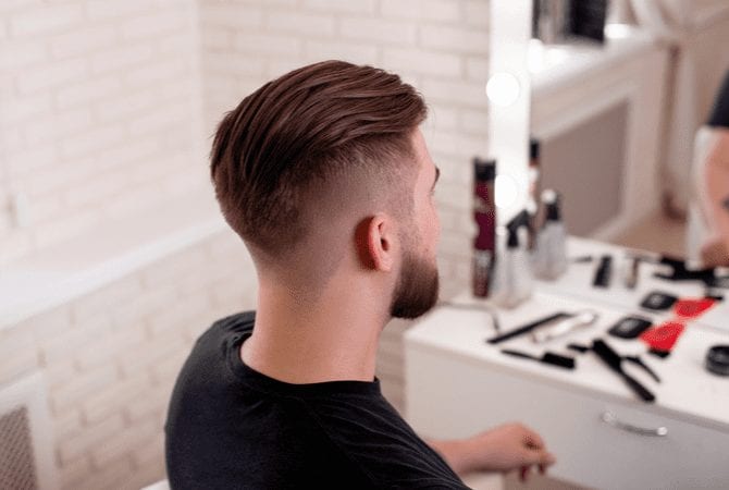 Guy with a high drop skin fade sits in a black shirt and looks into a mirror for a post on types of fades