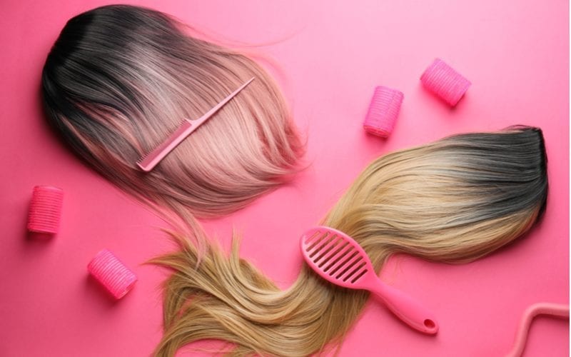 For a piece on where to buy good wigs online, two hairpieces sit alongside rollers and pink hair tools on top of a lay flat pink backdrop