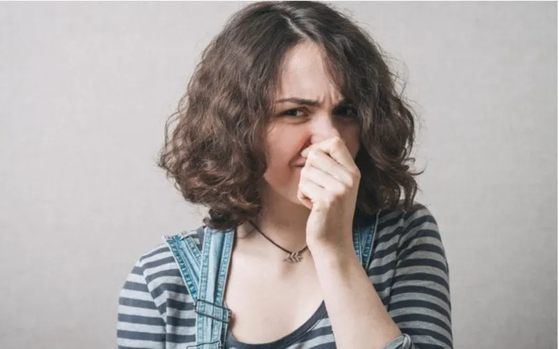 Hipster girl in overalls holding her nose because she didn't know if shampoo expires