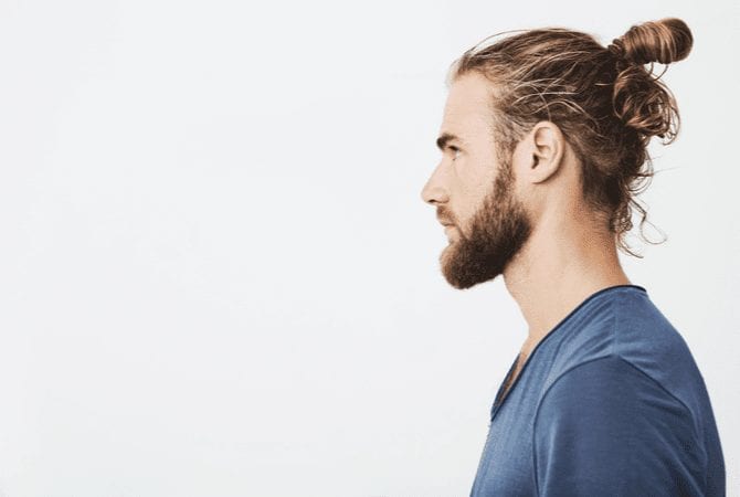 Man with a messy man bun standing in a side profile and looking away from the camera seriously
