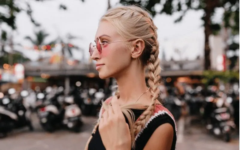 Hot woman with double french braids stands pensively holding one of the tips of her hair
