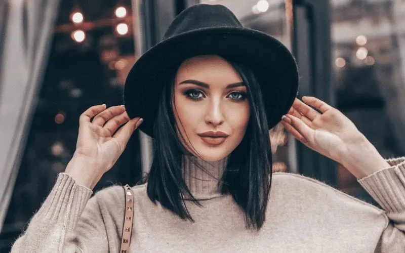 Gal with a lob haircut and a boho hat with a turtleneck sweater holds her hair