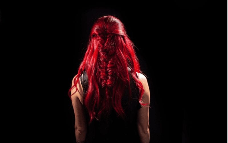 Woman with Ariel red hair stands and looks at a black wall