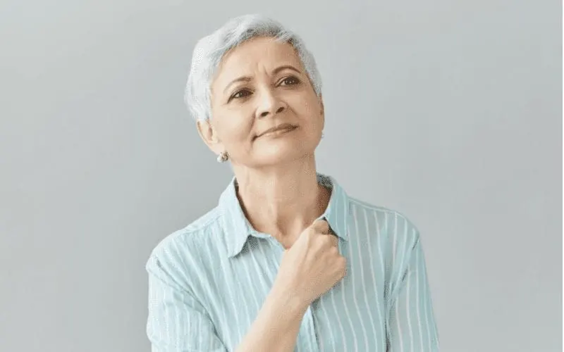 Pensive woman over 60 with a short haircut holding her right fist to her chest