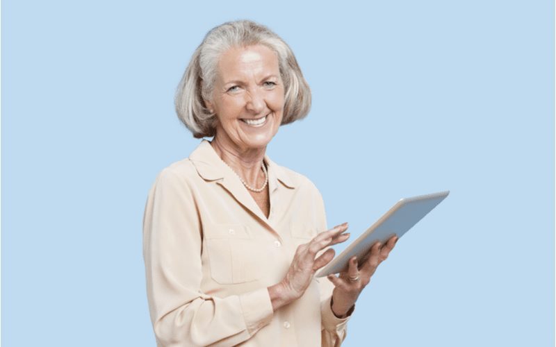 Older woman with a Blunt Cut Bob holding an ipad and smiling in a blue room