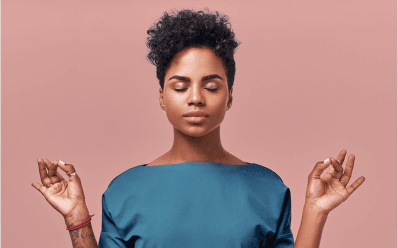 Meditating woman holding her hands in an O and wearing a short curly hairstyle