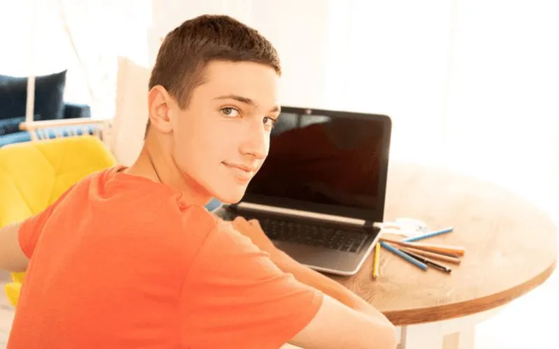 Short Crop on a guy in an orange shirt in front of a laptop for a piece on boys haircuts