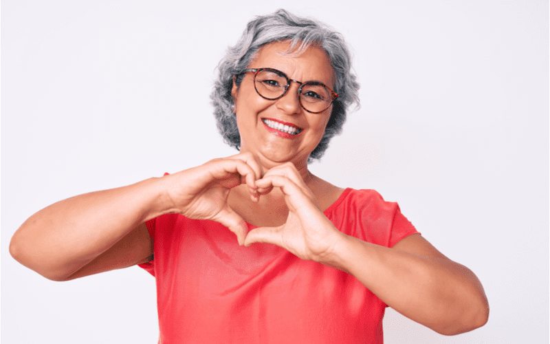 Older woman making a heart with her hands and wearing a Short Curly Cut With Bangs