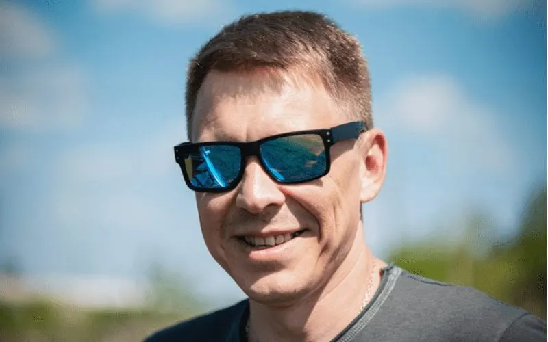 Guy with a mens short haircut stands looking at the camera in sunglasses