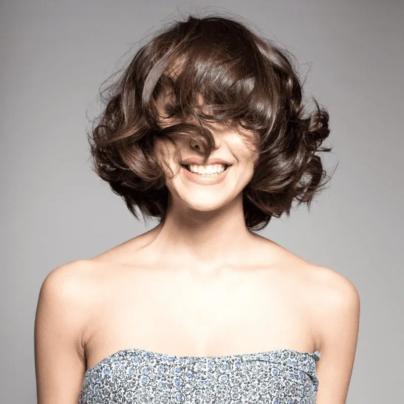 To help answer what is a lob haircut, a woman in a strapless dress stands with her bangs over her eyes