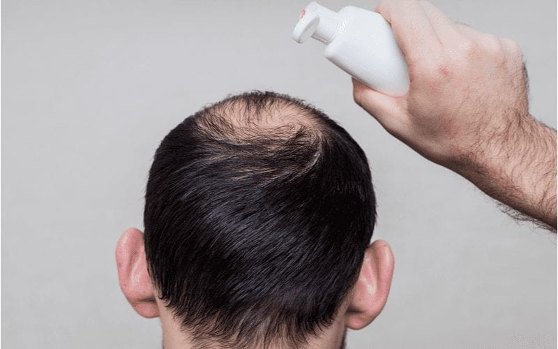Image of a man pouring the best shampoo for hair loss on his head in a studio, as viewed from behind
