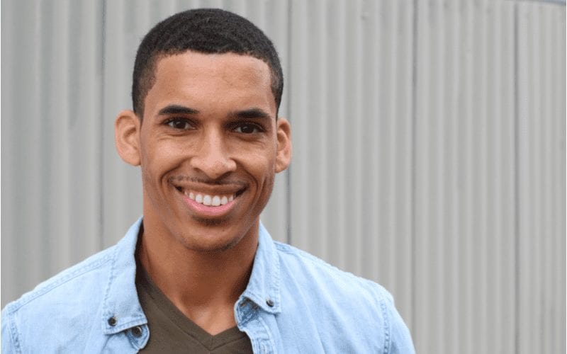 African American man in a blue open shirt smiles and has a short mens haircut