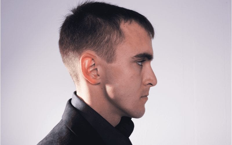 Side profile of a man in a black jacket in a studio with a mens short haircut