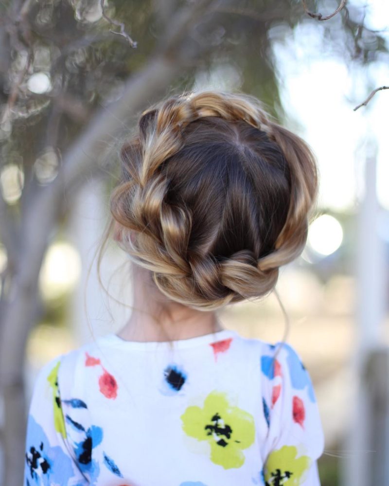 Braided crown hairstyle on a toddler in a floral shirt standing in front of a tree