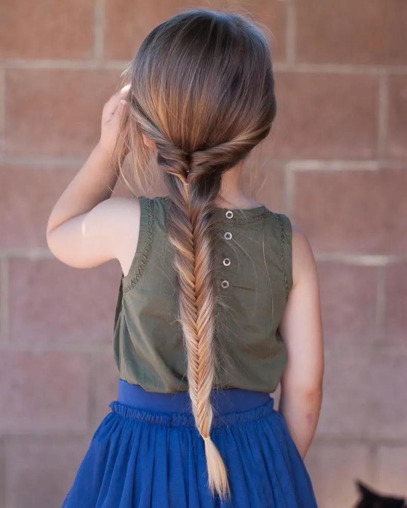 Twisted fishtail braided hairstyle on a young woman in a blue dress and grey shirt