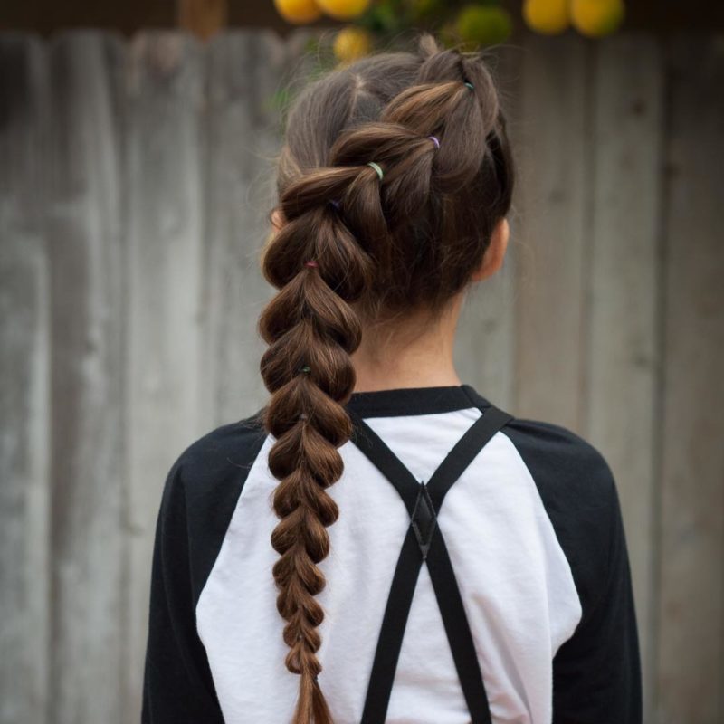 Diagonal pull through toddlers braided hairstyle on a woman in suspenders wearing a black and white baseball shirt