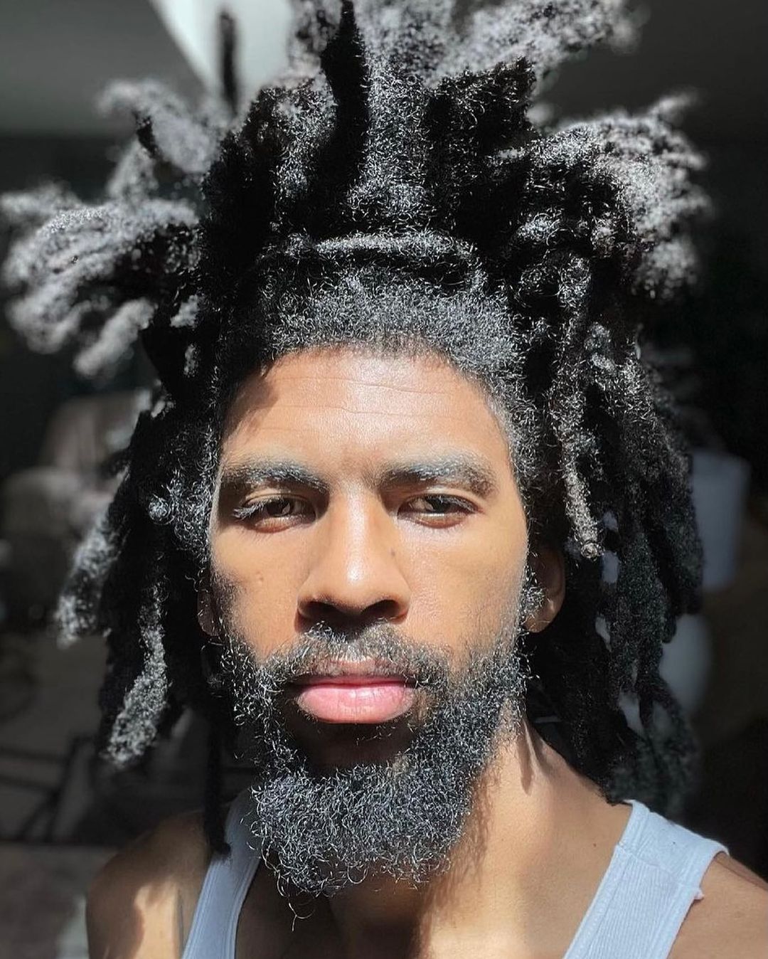 Man with fuzzy freeform locs in a white tank top and really letting his thick hair flow