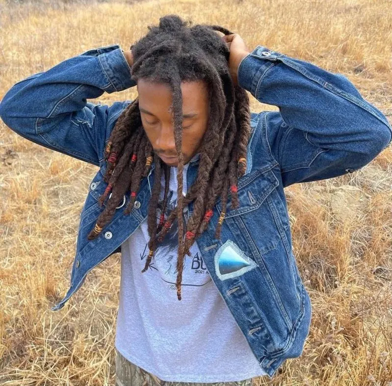 Man with freeform dreads holds his hands above his head