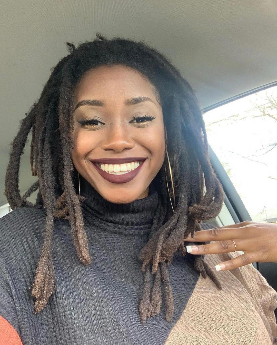 Woman with matted dreads smiles and holds her left hair roots