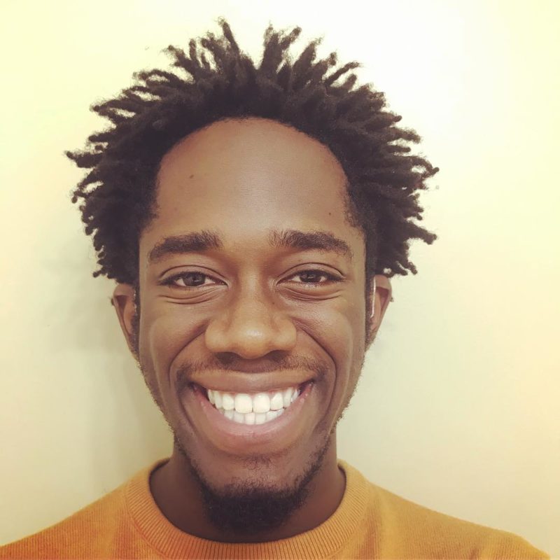 Man with short freeform dreads smiles big at the camera